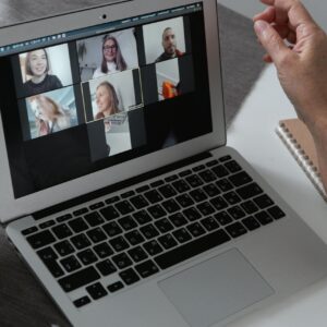 Hands at a laptop showing a group video call in a home office setting.